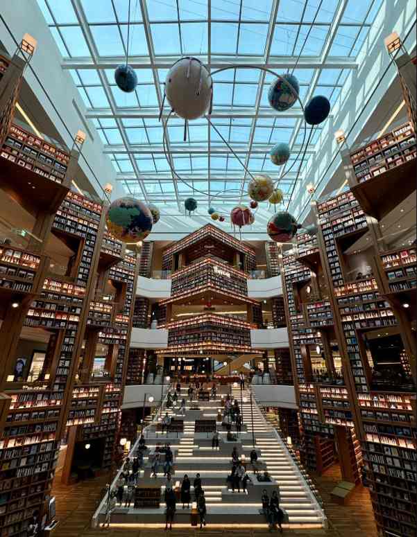 Suwon Starlight Library: una biblioteca espectacular en Corea del Sur Interior de la Suwon Starlight Library, con estanterías llenas de libros, una gran escalera central y planetas suspendidos bajo un techo de cristal.
