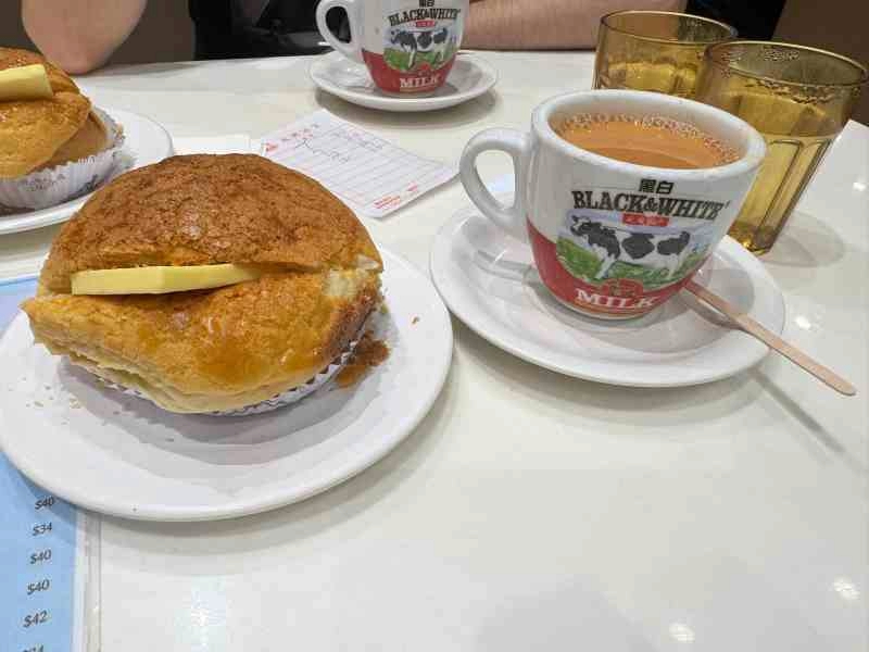 Pineapple bun de Hong Kong con una gruesa porción de mantequilla en su interior, acompañado de una taza de milk tea servida en una taza de Black & White.